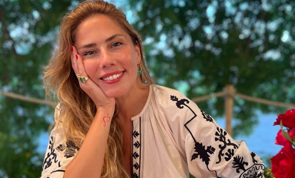 Gülümseyen sarı saçlı kadın işlemeli beyaz bluzu ve takılarıyla poz veriyor