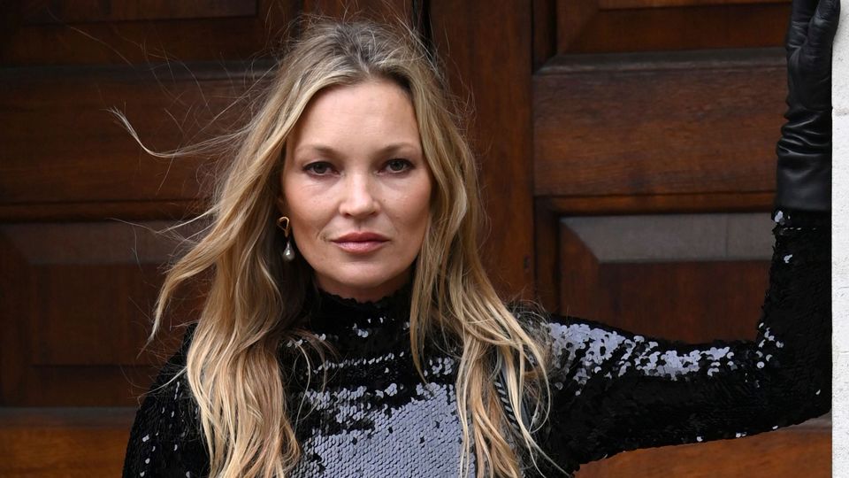 Kate Moss siyah pullu üstü ve uzun saçlarıyla kameraya bakıyor