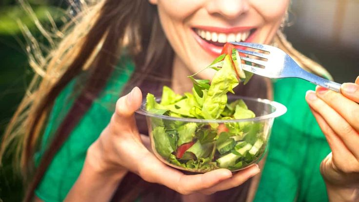 Gülümseyen kadın plastik kaseden çatalıyla salata yiyor