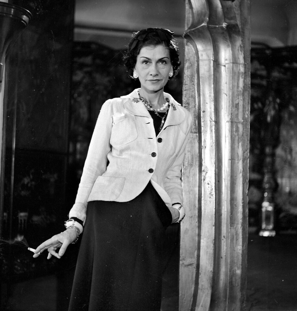 Siyah beyaz Coco Chanel portresi, ceket giymiş, sigara tutarken ciddi