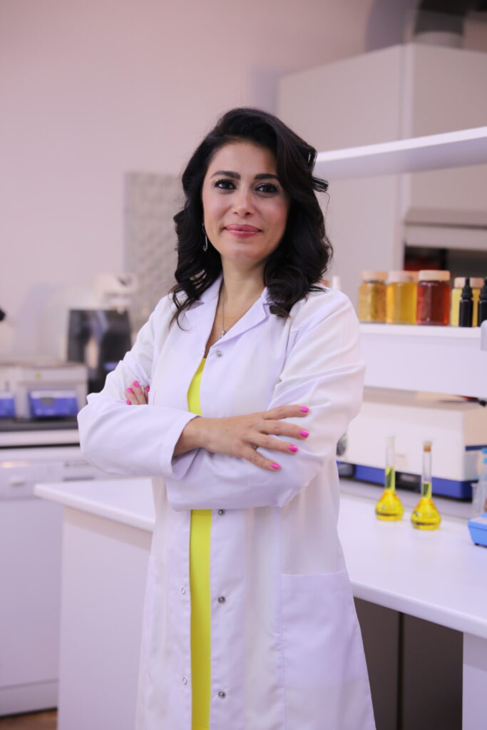 Laboratuvarda beyaz önlüklü gülümseyen bir kadın kollarını çaprazlamış