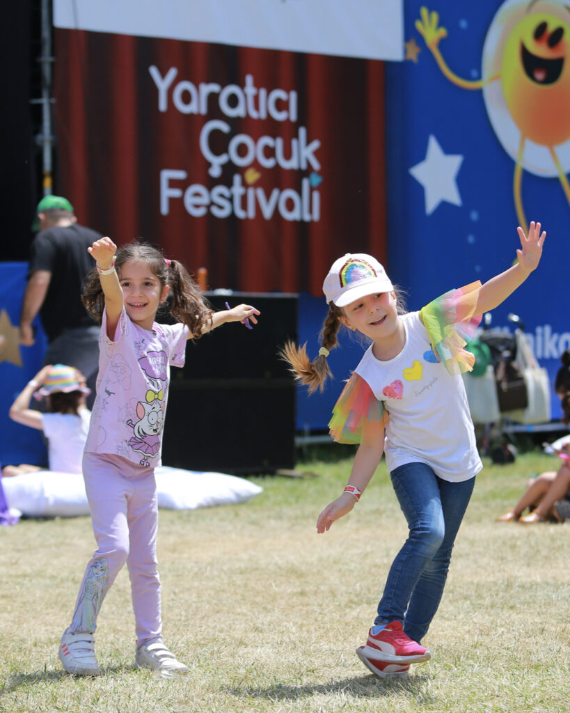 Yaratıcı Çocuk Festivali'nde çimlerde eğlenen iki mutlu kız çocuğu