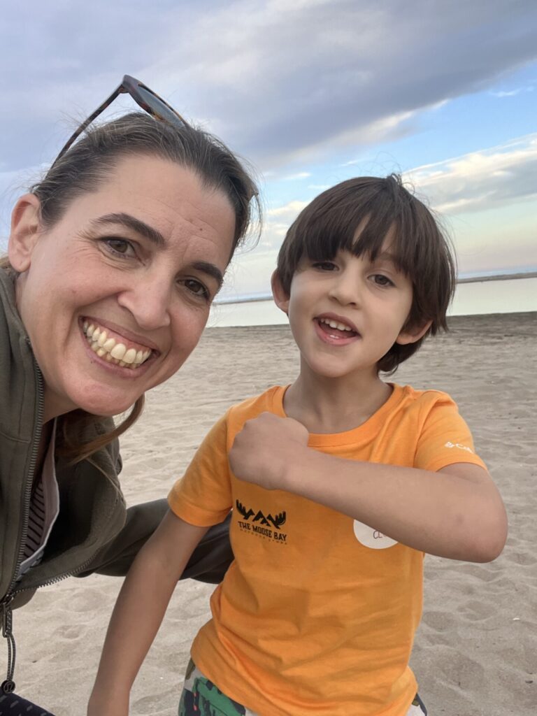 Gülümseyen bir kadın ve çocuk kumlu plajda selfie çekiyor