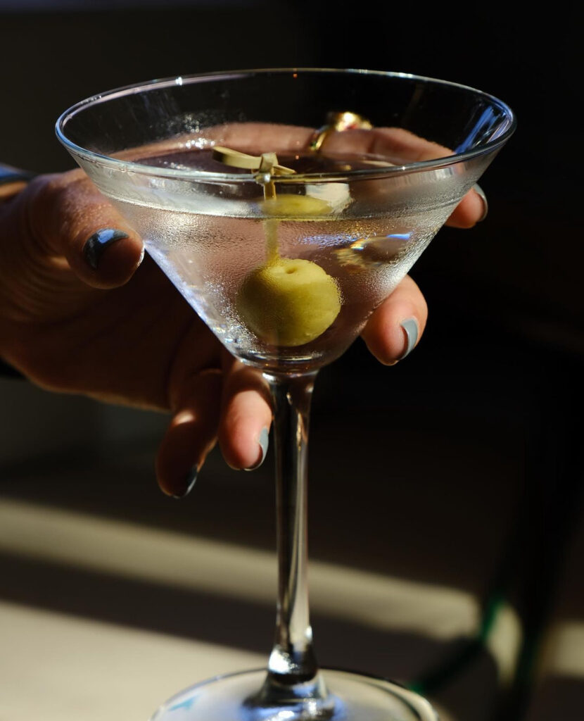 Koyu fonda zeytinli martini kadehini tutan bir el