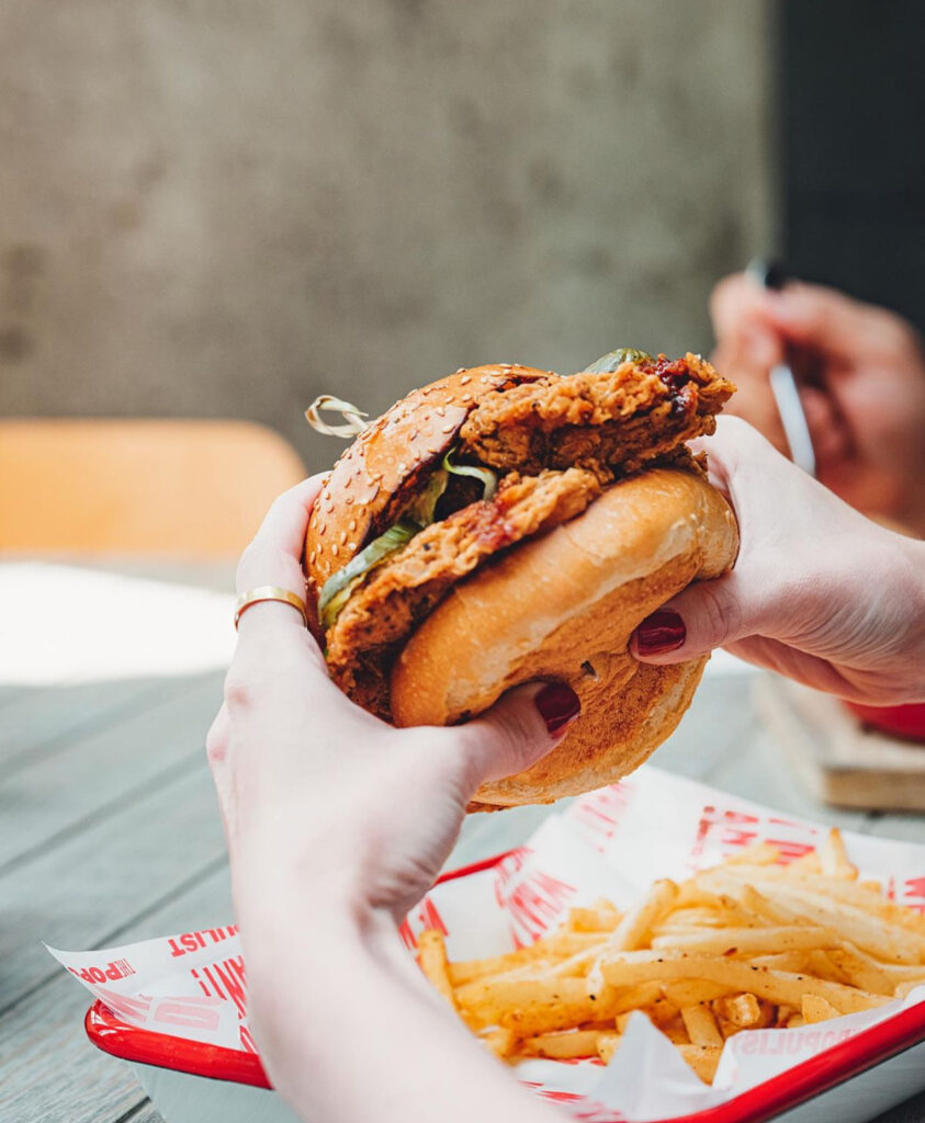 Çıtır tavuk burger ellerde tutulurken yanında patates kızartması