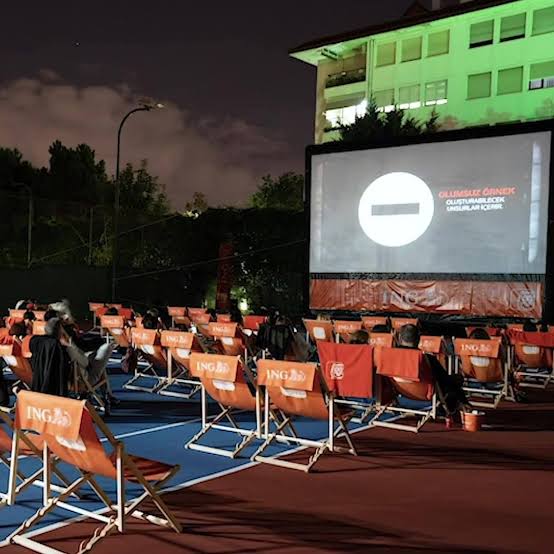 Tenis kortunda gece açık hava sinemasında film izleyen seyirciler
