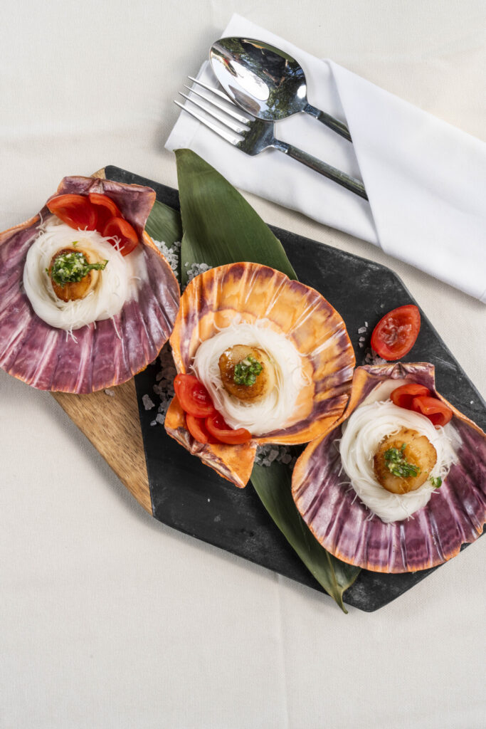 Noodle ve domatesli üç deniz tarağı kabuklarında bir servis tahtası üzerinde