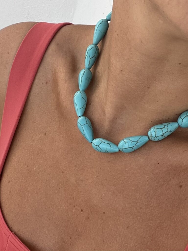 Turkuaz boncuklu kolye takmış bronz tenli bir kişinin omuzu