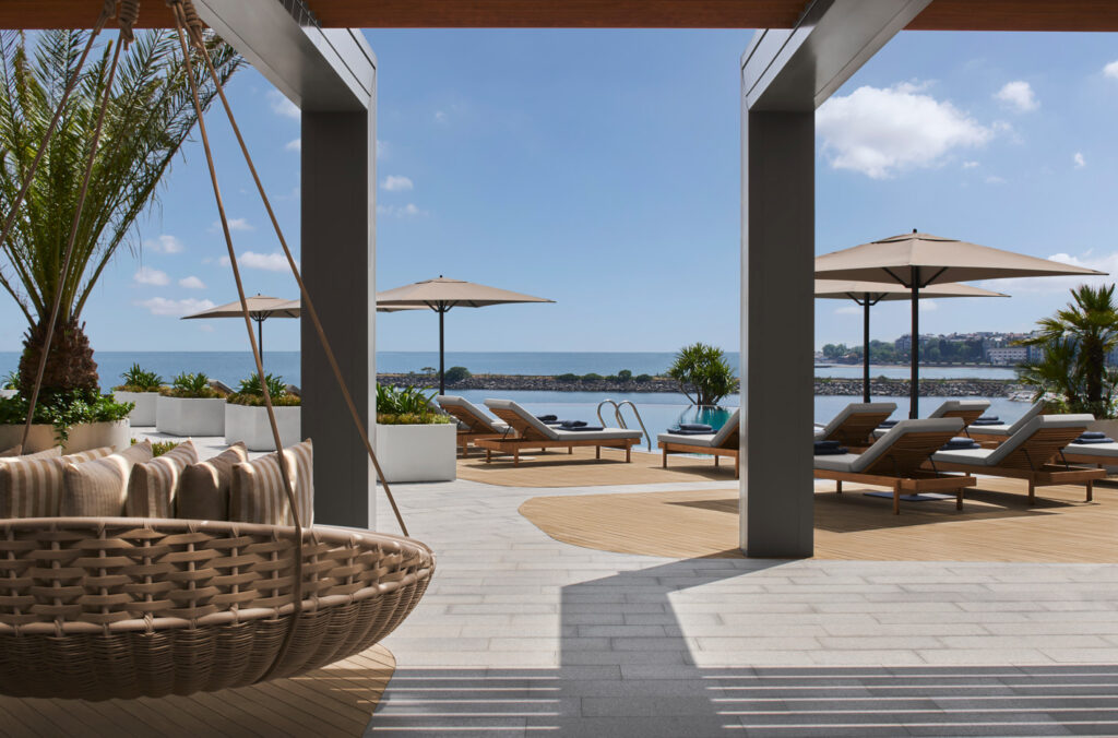 Havuz kenarında okyanus manzaralı, asılı sandalye ve şezlonglu modern otel terası