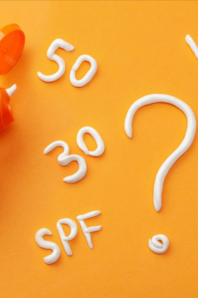 Güneş kremiyle yazılmış SPF 50, 30 ve soru işareti turuncu zemin üzerinde