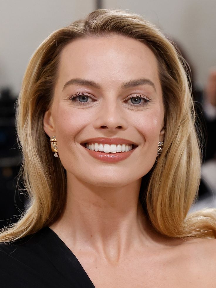 Margot Robbie'nin sarı saçlı, gülümseyen ve küpeli yakın çekim portresi