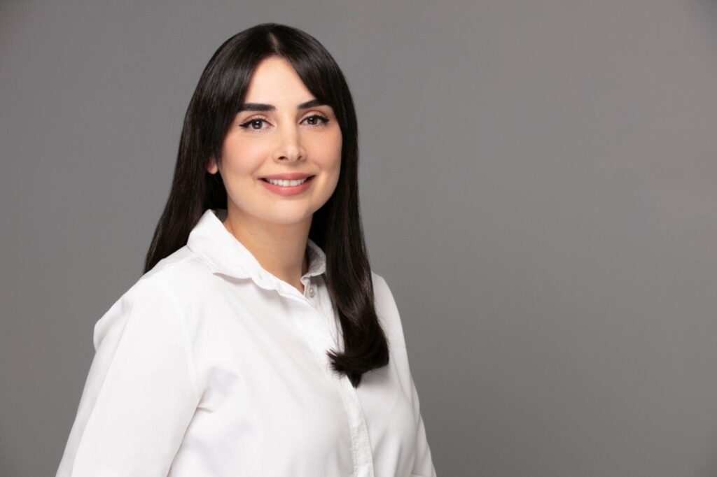 Beyaz gömlekli, gülümseyen genç bir kadın, gri arka planda