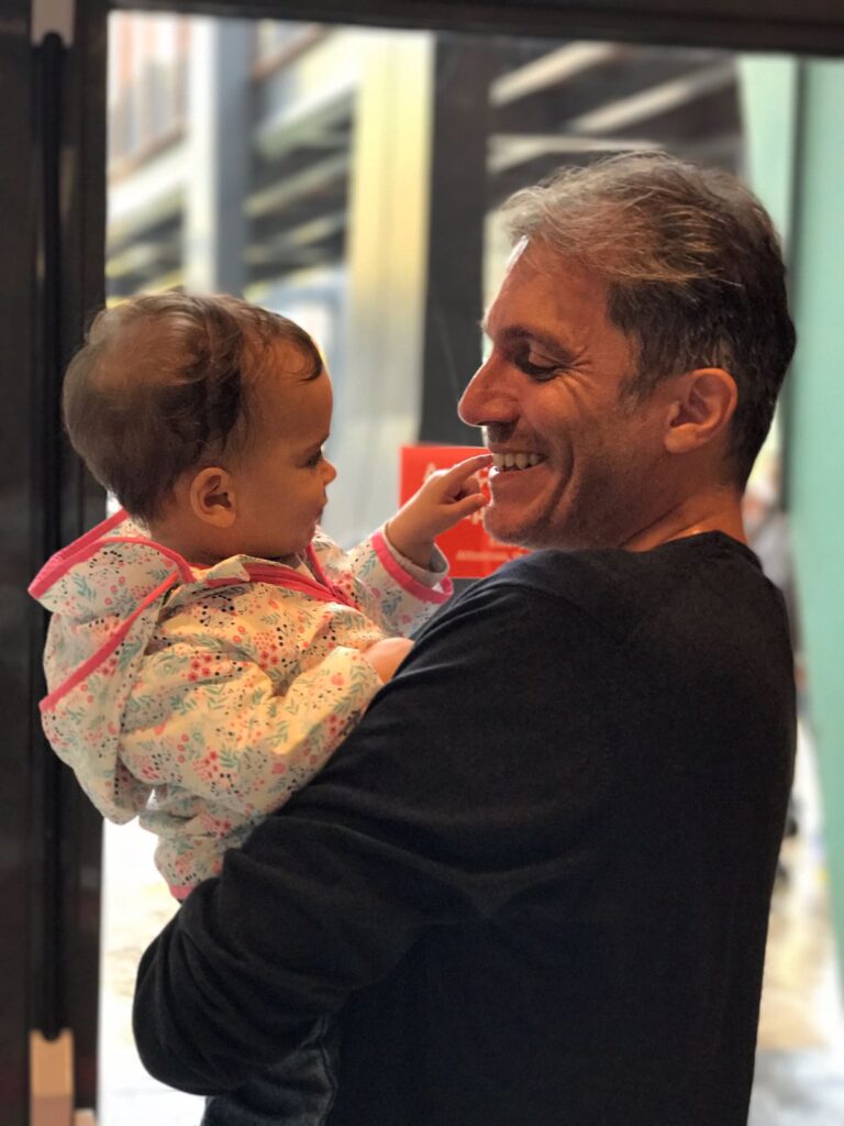 Kucağındaki bebek babasının ağzına dokunurken mutlu baba gülümsüyor