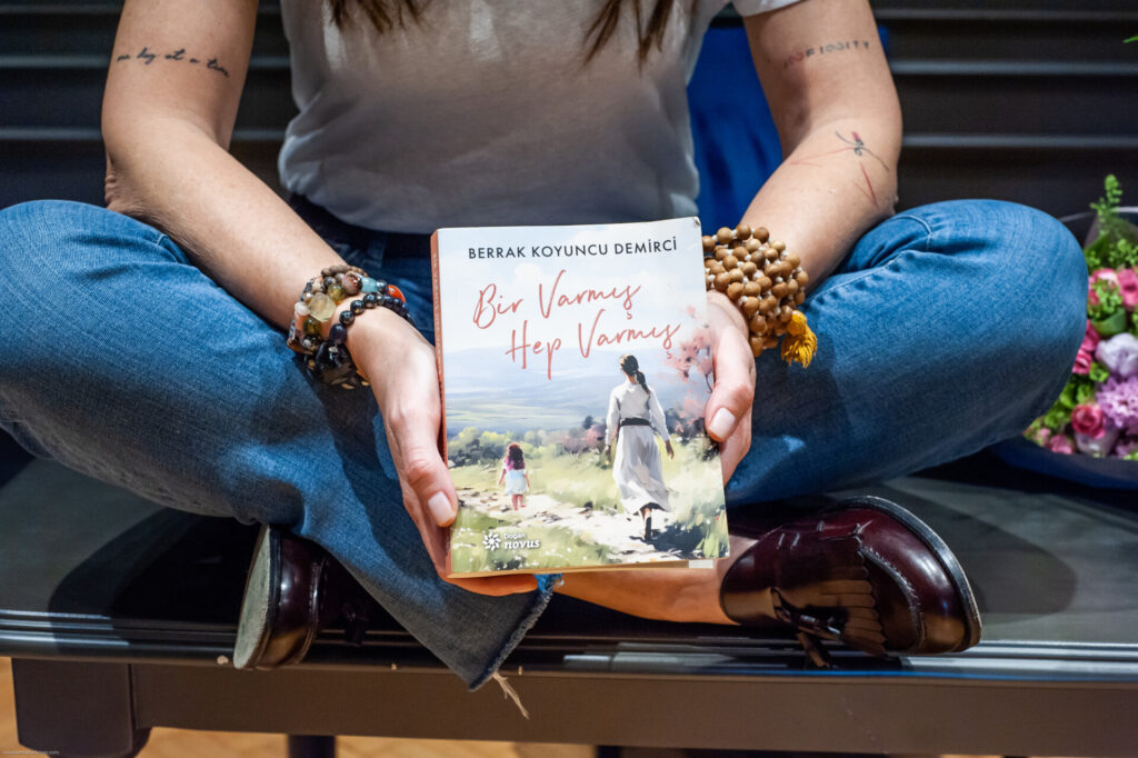 Kot pantolonlu birinin bağdaş kurmuş şekilde iki eliyle kitap tutması
