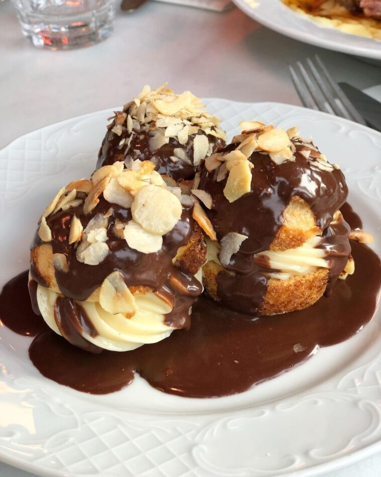 Çikolata sosu ve badem dilimleriyle süslenmiş kremalı profiterol tatlıları beyaz tabakta