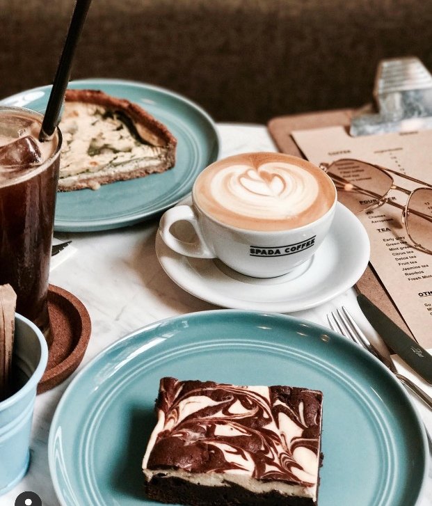 Bir kafe masasında latte, buzlu kahve, kiş ve brownie ikramları