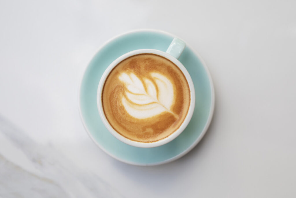 Mavi fincanda yaprak desenli latte sanatı beyaz zeminde üstten görünüm