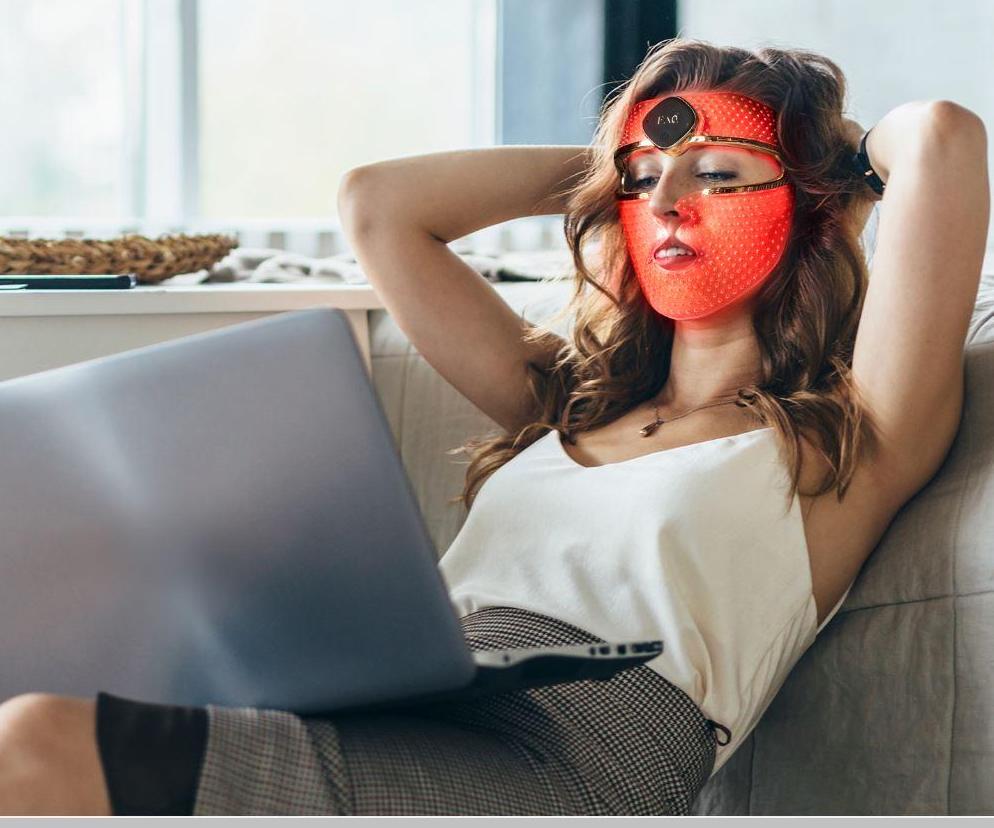 Kırmızı LED yüz maskesi takan kadın kanepede laptopla dinleniyor