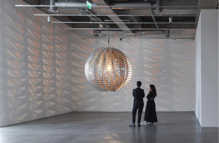 Sanat galerisinde dev bir küre avizeye bakan iki ziyaretçi