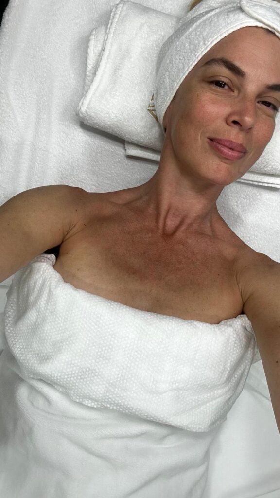 Spa havlularına sarılı rahatlamış bir kadın yüz bakımı için uzanıyor