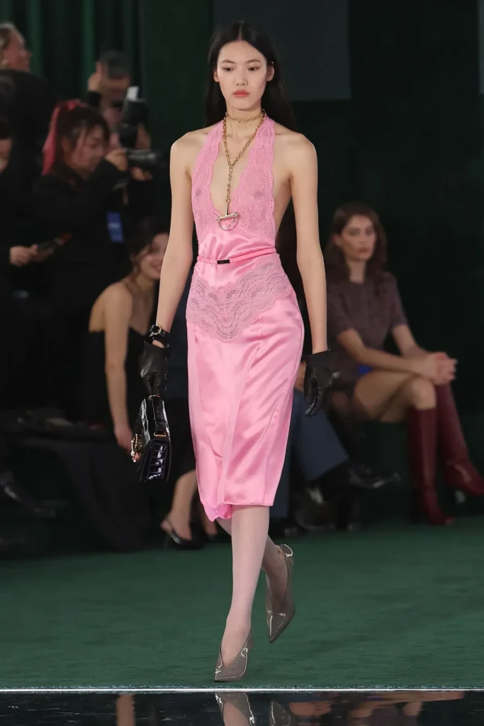 Podyumda pembe dantel slip elbise, siyah eldiven ve çantalı model