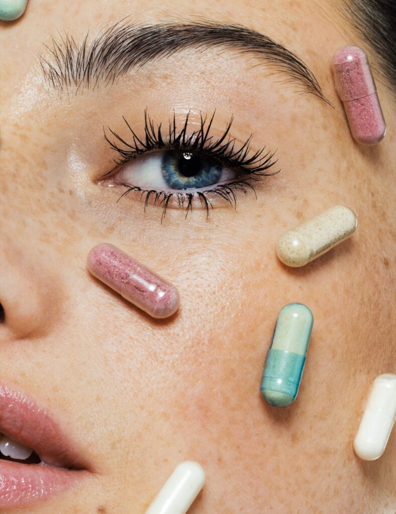 Çilli kadın yüzü, mavi göz ve renkli vitamin kapsülleri