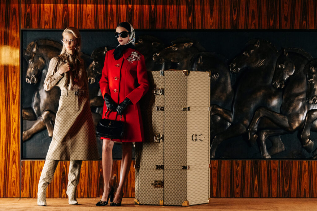 Lüks Gucci kıyafetli iki model, bavul ve at kabartmalı duvar önünde