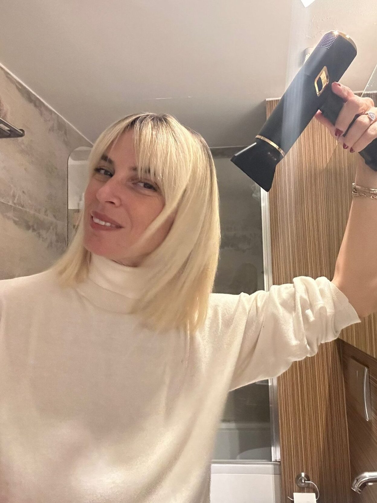 Sarışın kadın saç kurutma makinesiyle banyoda neşeli bir selfie çekiyor