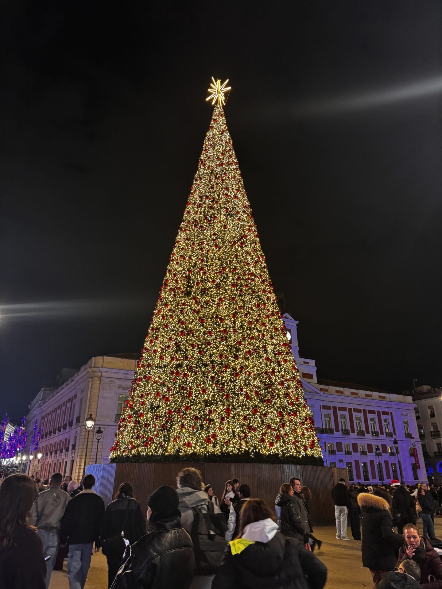 Gece şehir meydanında devasa ışıklı Noel ağacı ve kalabalık