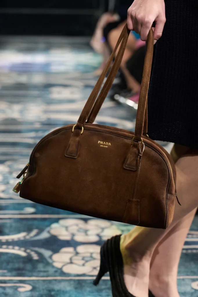 Kahverengi süet Prada çanta taşıyan bir kişi desenli zeminde