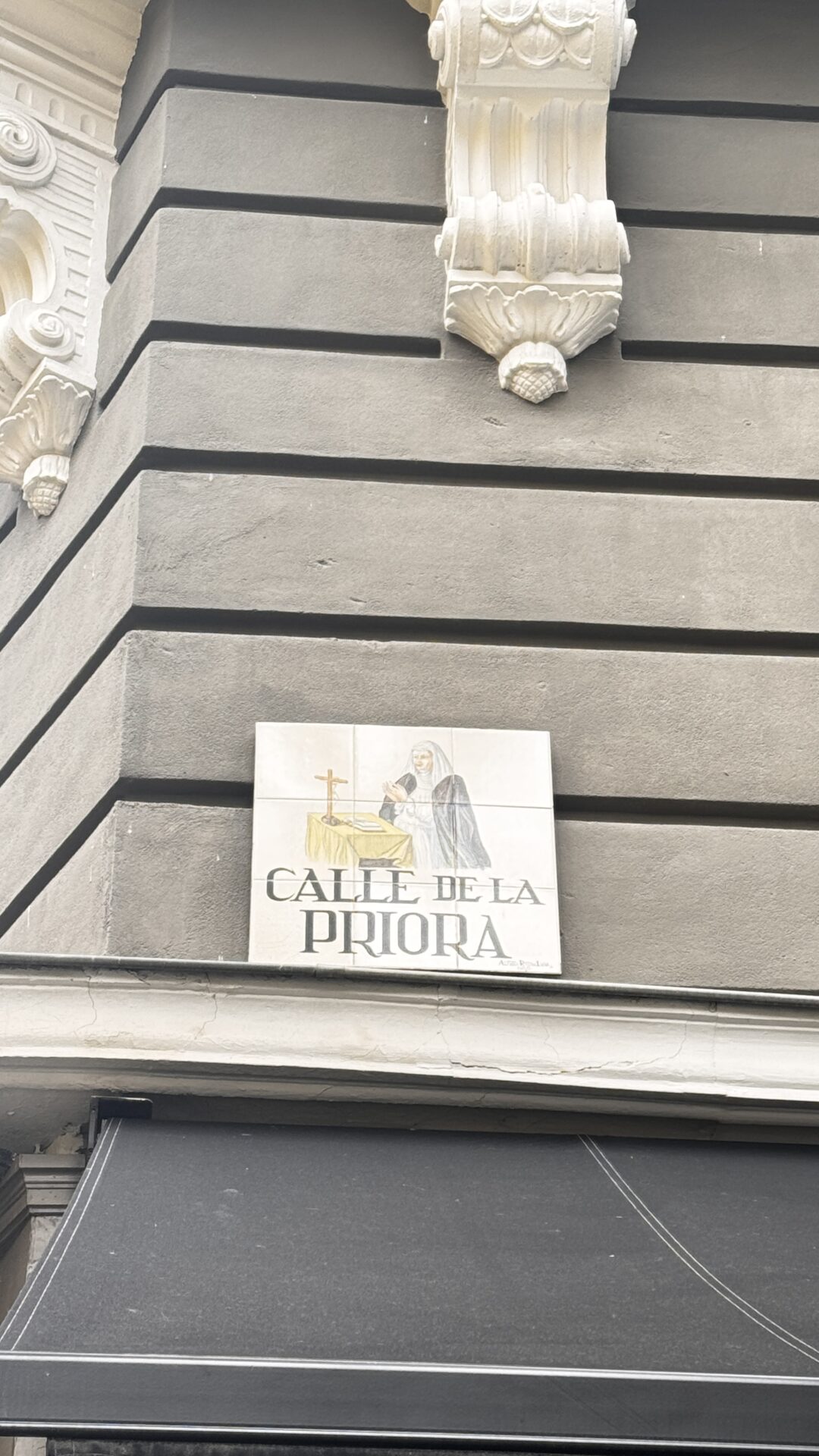 Gri duvarda rahibe resimli 'CALLE DE LA PRIORA' sokak levhası