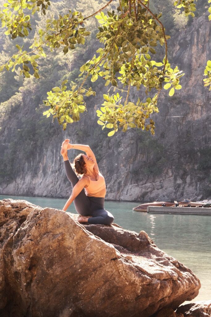 Doğal ortamda kayada yoga yapan kadın su ve dağ manzaralı