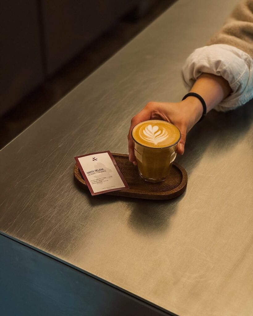 Parlak tezgah üzerinde latte sanatı olan kahve fincanını alan el