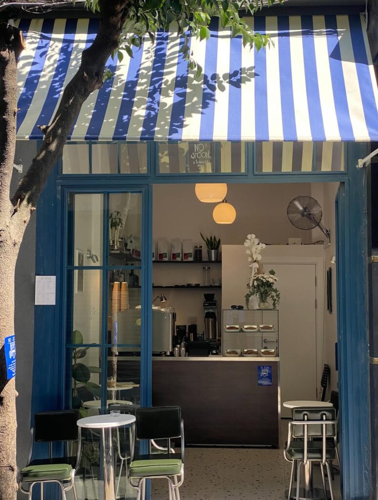 Ağaçlıklı mavi beyaz çizgili tenteli şirin kafe dış görünümü oturma alanıyla