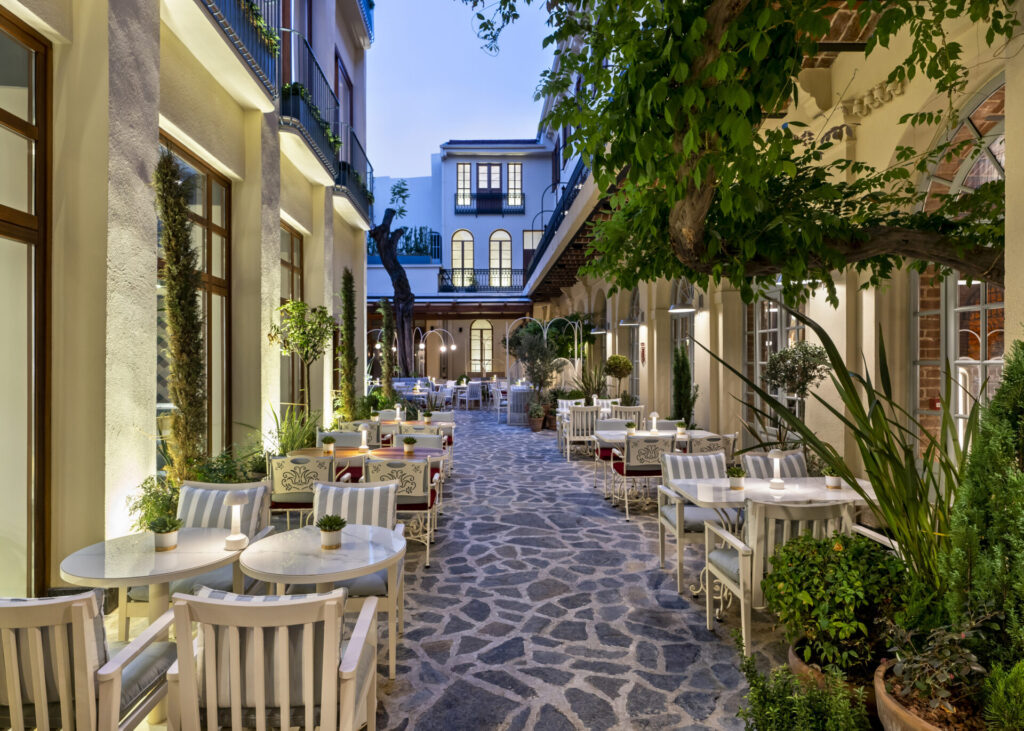 Taş zeminli avluda bitkiler ve masalarla dolu şık bir restoran