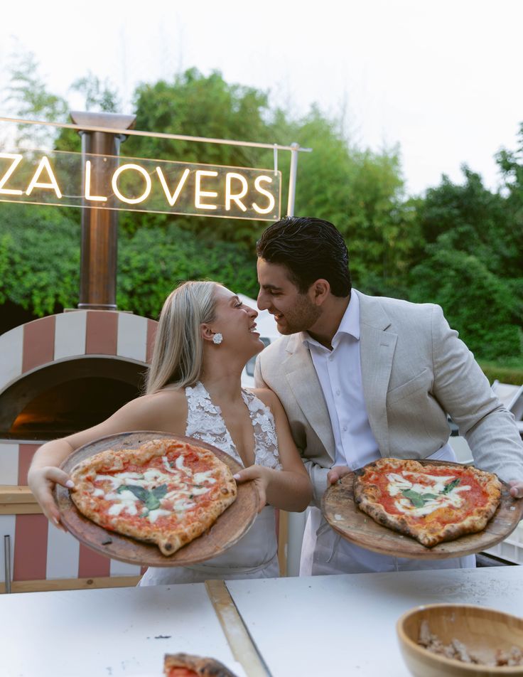 Aşıklar kalp pizzalarıyla pizza fırınının yanında gülümseyerek bakışıyorlar