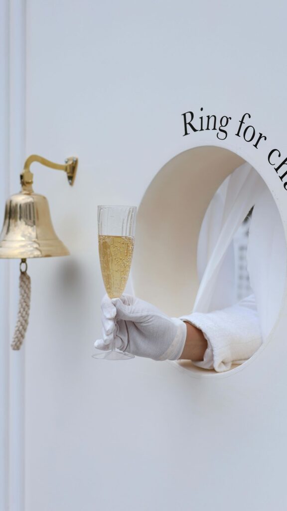 Altın zil, elinde şampanya kadehi tutan el, 'Ring for ch...' yazısı