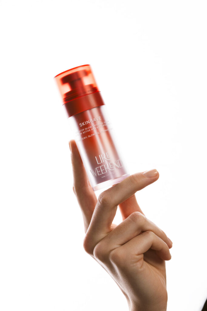 Elinde tutulan, "SKINRAVE LIKE WEEKEND" yazılı kozmetik serum şişesi